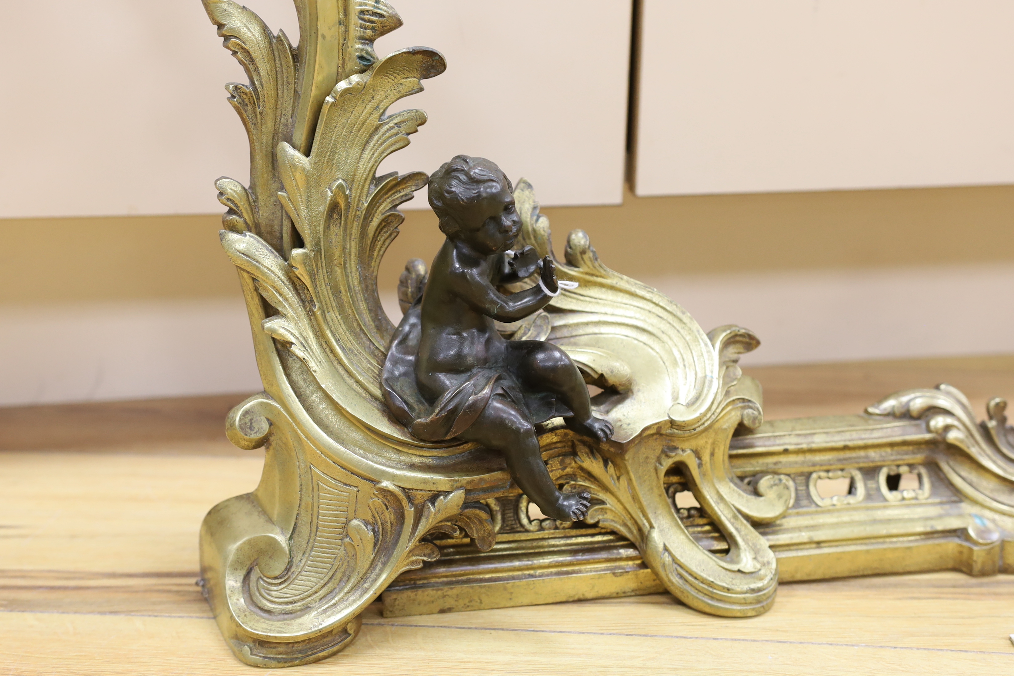 A pair of brass chenet mounted with patinated bronze figures of putti, 97cm wide